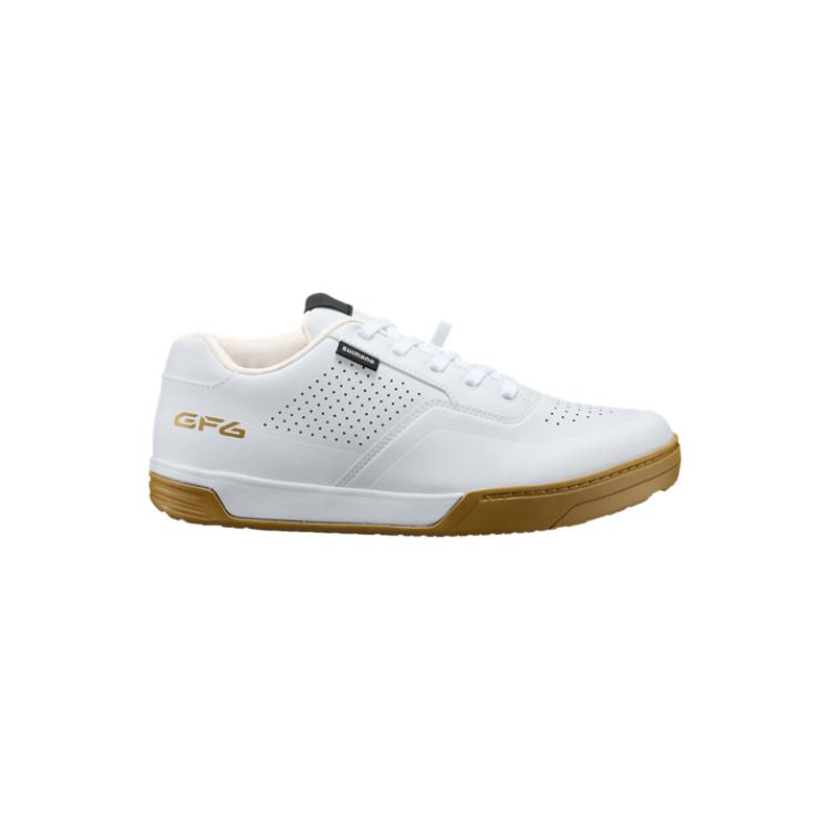White Shimano GF6 flat-pedal mountain bike shoe with a gum rubber outsole, shown in side, top, and sole views. The shoe features a durable synthetic upper with perforated ventilation panels, white laces, gold "GF6" branding on the heel, and a grippy hexagonal tread pattern designed for pedal traction. Displayed against a light gray background.