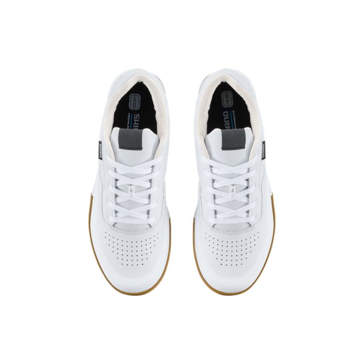 White Shimano GF6 flat-pedal mountain bike shoe with a gum rubber outsole, shown in side, top, and sole views. The shoe features a durable synthetic upper with perforated ventilation panels, white laces, gold "GF6" branding on the heel, and a grippy hexagonal tread pattern designed for pedal traction. Displayed against a light gray background.