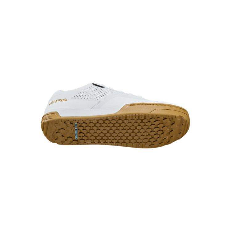White Shimano GF6 flat-pedal mountain bike shoe with a gum rubber outsole, shown in side, top, and sole views. The shoe features a durable synthetic upper with perforated ventilation panels, white laces, gold "GF6" branding on the heel, and a grippy hexagonal tread pattern designed for pedal traction. Displayed against a light gray background.