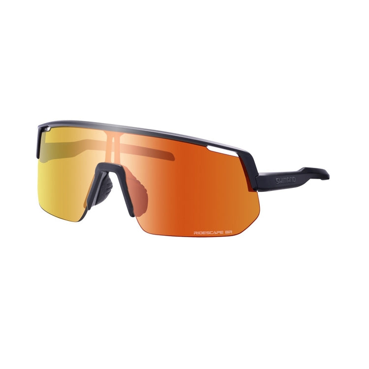 Three-quarter front view of Shimano performance cycling sunglasses featuring a large frameless shield lens with a mirrored orange-gold finish. The dark temple arm displays the Shimano logo, and the adjustable nose piece is visible against a light gray background.