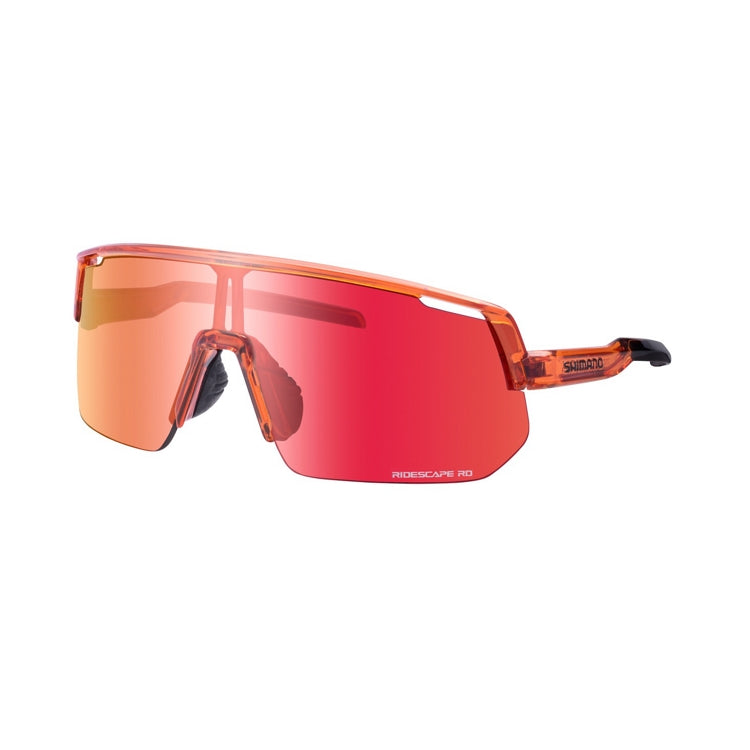 Three-quarter front view of Shimano performance cycling sunglasses with an oversized shield lens in a mirrored red-orange finish. The translucent orange frame, adjustable nose pads, and streamlined temple arm design are visible against a light gray background.