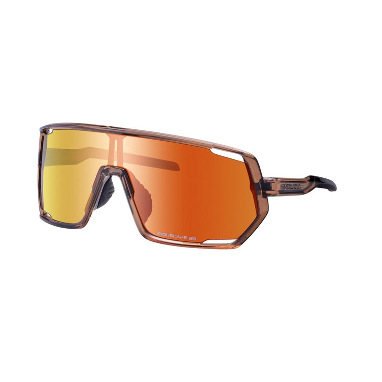 Three-quarter front view of Shimano performance cycling sunglasses with a wide shield lens in a mirrored gold-to-orange finish. The translucent brown full-rim frame features geometric corners, adjustable nose pads, and subtle cutout accents near the lens edges, shown against a light gray background.