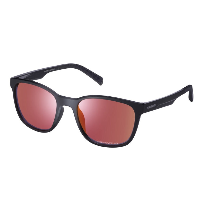 Matte black Shimano sunglasses with a lightweight full-rim frame and mirrored red-pink lenses, shown from front and side views on a light gray background. The rectangular lenses have gently rounded edges, while the slim black temples feature Shimano branding and textured temple tips for added grip. The reflective lenses display a vibrant rose-red finish with subtle purple tones around the lens edges.