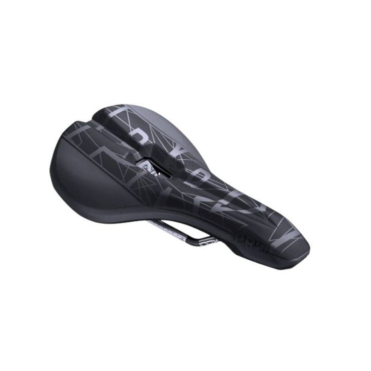 Three-quarter front view of a black bicycle saddle showing the contoured shape, central channel, and metal rails underneath. The top surface displays a dark geometric graphic pattern with large lettering in contrasting gray tones. The saddle is positioned against a light gray background.